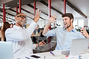 Two cheerful men giving high five and working in office