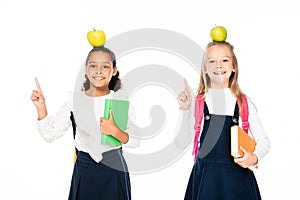 two cheerful multicultural schoolgirls with apples on heads showing idea gestures isolated on white.