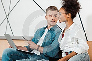 Two cheerful multiethnic students using laptop