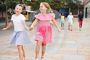 Two cheerful preteen girls enjoying walk along city street