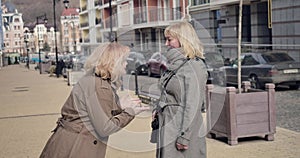 Two cheerful senior women talking on city street on sunny autumn day. Positive caucasian retirees enjoying pension