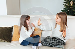 Two cheerful smiling girls sisters sitting on couch in living room while playing patty-cake game