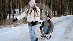 Two cheerful teenage girl riding on sleighs and having fun in winter forest