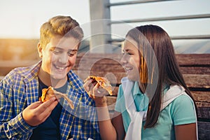 Two cheerful teenagers, girl and boy, eating pizza