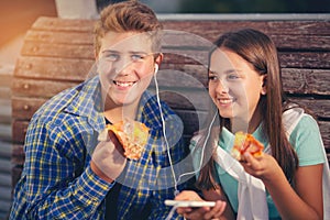 Two cheerful teenagers, girl and boy, eating pizza