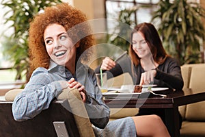 Two cheerful women sitting in cafe and laughing together