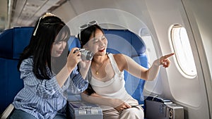 Two cheerful young Asian female friends are enjoying talking and taking pictures during the flight