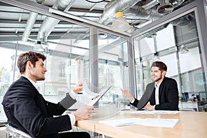 Two cheerful young businessmen creating business plan on meeting