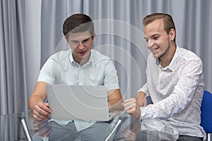 Two cheerful young businessmen working and using laptop on business meeting together