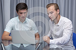 Two cheerful young businessmen working and using laptop on business meeting together