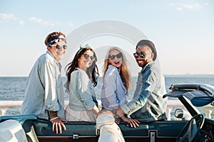 Two cheerful young couples standing near cabriolet