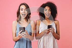 Two cheerful young girl in dresses holding mobile phones