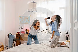 Two young girls holding brushes as microphones and singing songs on bed