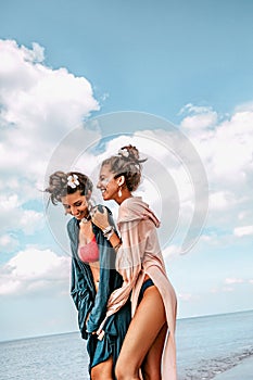 Two cheerful young stylish woman twin sisters having fun on the beach