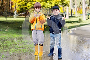 Two cheerfull boys in rubber boots standing in puddle in park. Concept of social adaptation of autistic children
