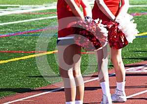 Two cheerleaders holding their red and white pom poms bshind their back