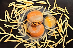 Two cheeseburgers, french fries scattered on a wooden dark table and mustard