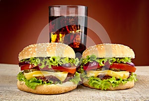 Two cheeseburgers,glass of cola on wooden table on red spotlight