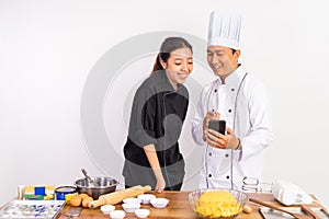 two chefs smiling while using mobile phones standing near table