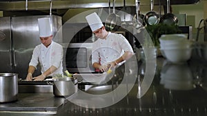 Two chefs in white uniforms work in a large professional kitchen.