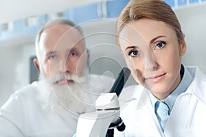 Two chemists in white coats working with microscope and looking at camera