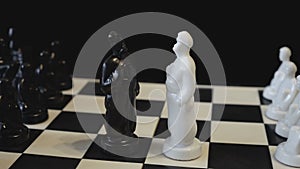 Two chess kings, black and white, face each other on a rotating black-and-white chessboard. Chess pieces in the form of