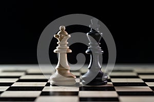 Two chess pieces, white queen and black king side by side on a chessboard against a dark background, concept for diversity, gender