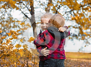 Two child boys in identical red shirts in a cage are hugging in an autumn park