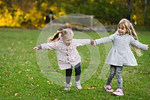 Two child girls play on the lawn in the autumn park