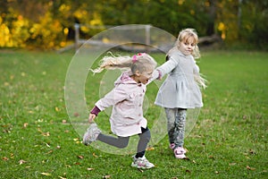 Two child girls play on the lawn in the autumn park