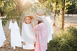 Two child girls playing having fun hanging white bed sheets on rope outdoor.