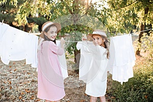 Two child girls playing having fun hanging white bed sheets on rope outdoor.