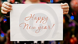 Two child`s hands hold a piece of paper with a congratulation happy new year