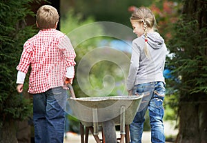 Two Childen Playing With Wheelbarrow In Garden