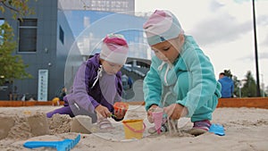 Two children 4-5 years old sitting in sandbox, playing with toys and buckets