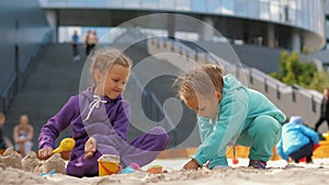 Two children 4-5 years old sitting in sandbox, playing with toys and buckets