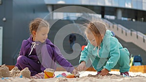Two children 4-5 years old sitting in sandbox, playing with toys and buckets