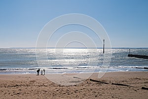 Two children and an adult play on a beach on a bright spring day. The sea is shimmering in the sunshine