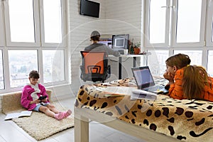 Two children and an adult work in different electronic devices at home
