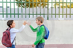 Two children with backpacks on their backs greet each other with high fives. Back to school concept