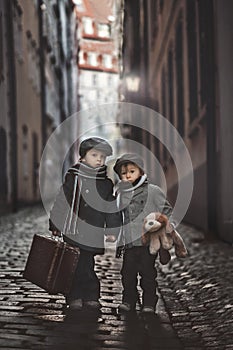 Two children, boy brothers, carrying suitcase and dog toy, travel in the city alone