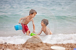 Two children, boy brothers, playing on the beach with sand toys