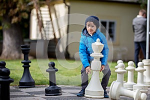 Two children, boy brothers, playing chess with huge figures in t