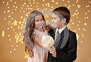 Two children boy and girl are in christmas lights, yellow background, winter holiday concept
