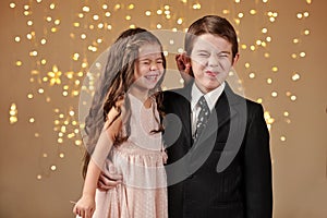 Two children boy and girl are in christmas lights, yellow background, winter holiday concept