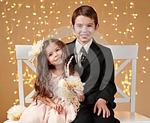 Two children boy and girl are in christmas lights, yellow background, winter holiday concept