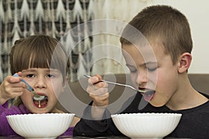 Two children boy and girl eating soup with spoon from a plate wi