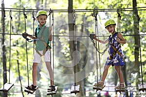 Two children, boy and girl in protective harness and safety helmets at climbing activity on rope way