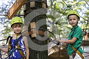 Two children, boy and girl in protective harness and safety helmets at climbing activity on rope way