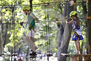 Two children, boy and girl in protective harness and safety helmets at climbing activity on rope way